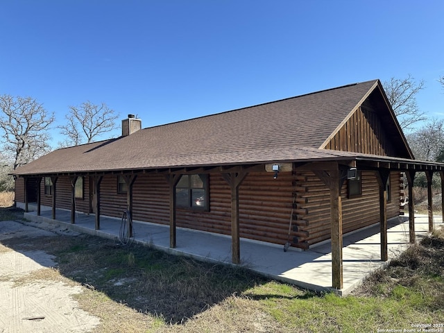 view of property exterior with a chimney, log siding, and roof with shingles