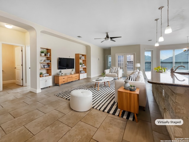 tiled living area featuring baseboards, arched walkways, a ceiling fan, and french doors