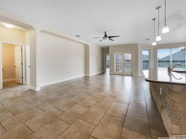 unfurnished living room featuring arched walkways, french doors, light tile patterned flooring, ceiling fan, and baseboards