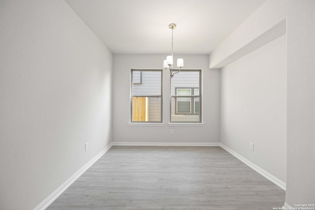 unfurnished room with baseboards, a chandelier, and wood finished floors