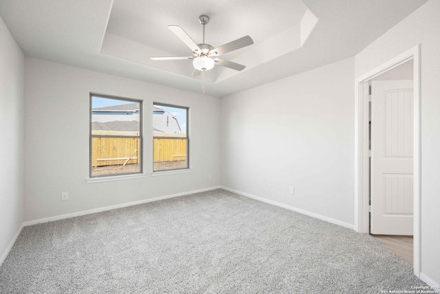 carpeted empty room featuring ceiling fan, a raised ceiling, and baseboards