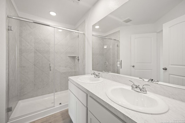 bathroom featuring double vanity, wood finished floors, a sink, and a shower stall