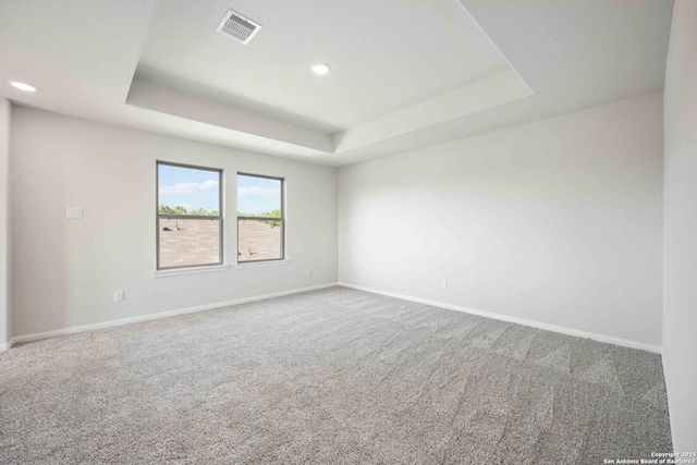 empty room with baseboards, visible vents, a tray ceiling, and carpet flooring