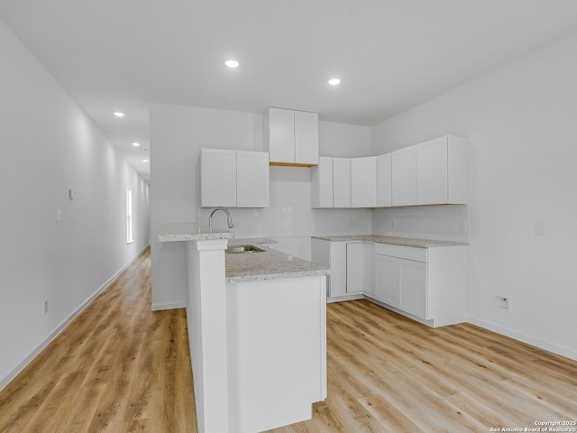 kitchen with light wood-style floors, tasteful backsplash, white cabinets, and a sink