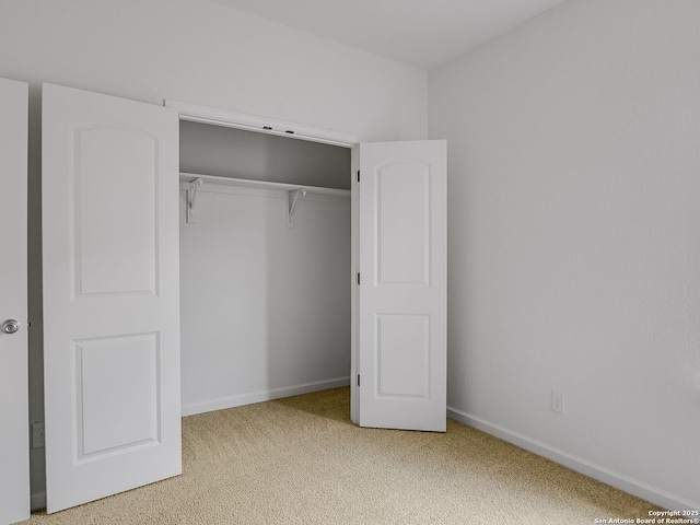 interior space featuring a closet, light colored carpet, and baseboards