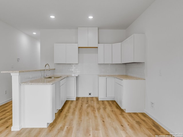 kitchen with light stone countertops, light wood-style flooring, white cabinets, and a sink