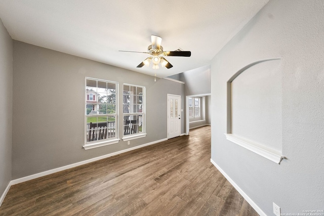 unfurnished room with plenty of natural light, wood finished floors, a ceiling fan, and baseboards