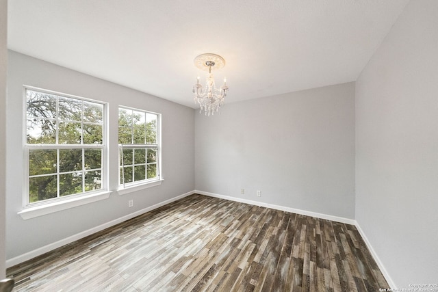 spare room featuring baseboards, wood finished floors, and an inviting chandelier