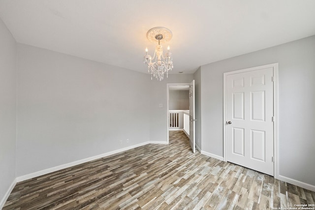 spare room featuring baseboards, a notable chandelier, and wood finished floors