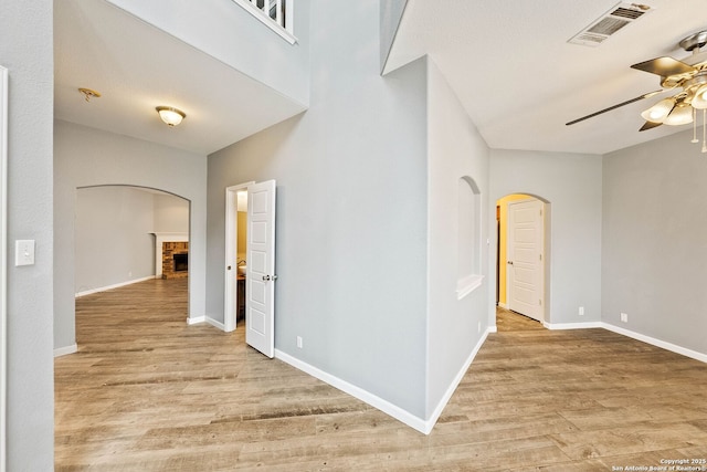 interior space with arched walkways, light wood finished floors, visible vents, a brick fireplace, and ceiling fan