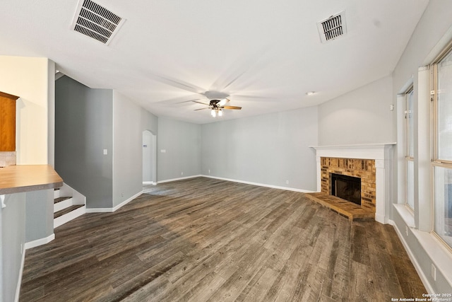 unfurnished living room with a brick fireplace, a ceiling fan, visible vents, and wood finished floors