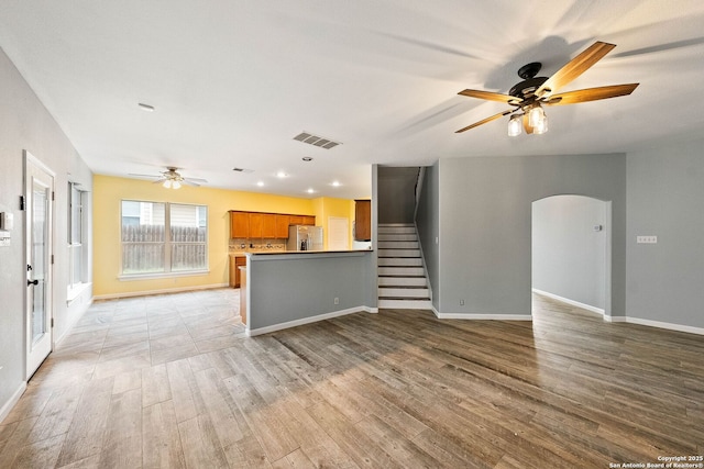 unfurnished living room with arched walkways, visible vents, light wood-type flooring, baseboards, and stairs