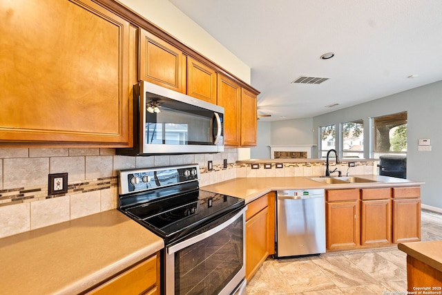 kitchen with a peninsula, a sink, visible vents, appliances with stainless steel finishes, and brown cabinetry