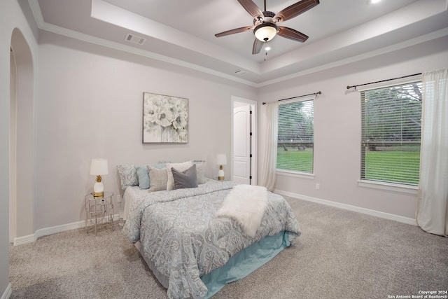 carpeted bedroom with arched walkways, a tray ceiling, visible vents, and baseboards