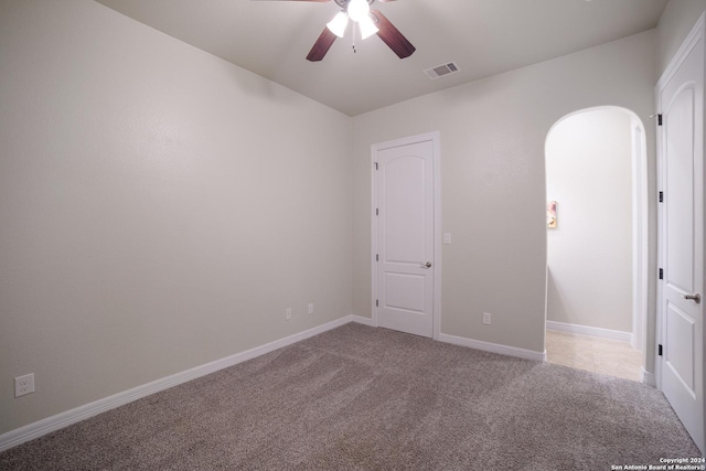 carpeted empty room featuring baseboards, arched walkways, visible vents, and a ceiling fan