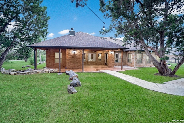 back of house with a yard, brick siding, a chimney, and roof with shingles