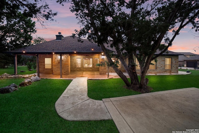 back of house at dusk with a yard, a chimney, and stone siding