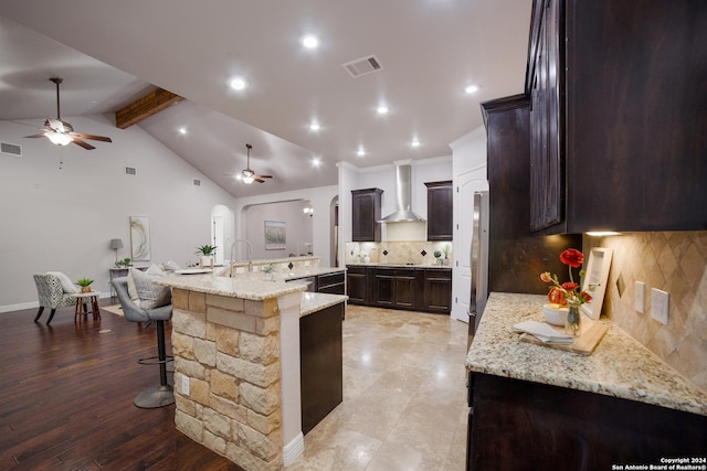 kitchen featuring wall chimney exhaust hood, a large island, backsplash, and visible vents