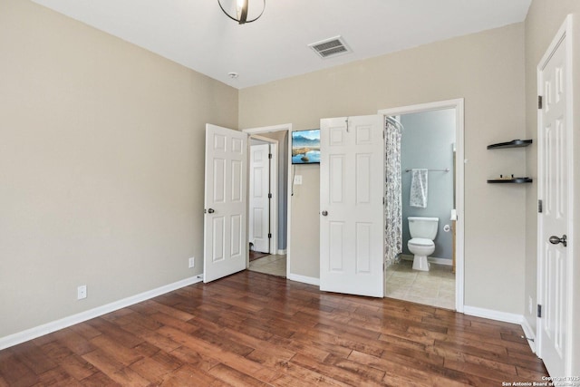 unfurnished bedroom featuring baseboards, connected bathroom, visible vents, and wood finished floors