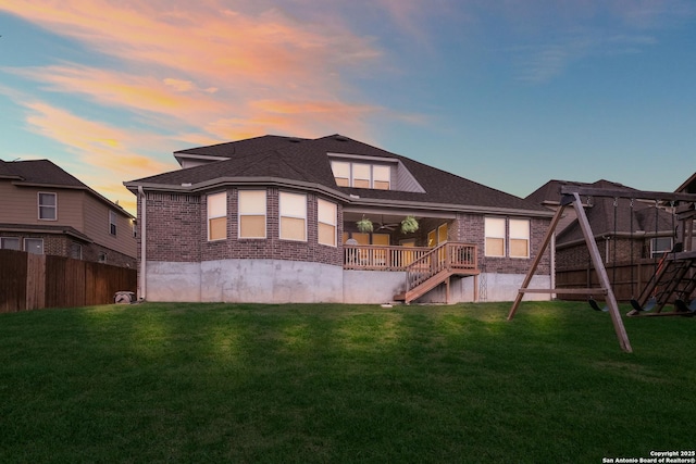 back of house at dusk with brick siding, a lawn, and fence