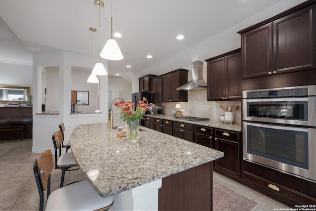 kitchen with light stone counters, a breakfast bar, backsplash, appliances with stainless steel finishes, and wall chimney range hood