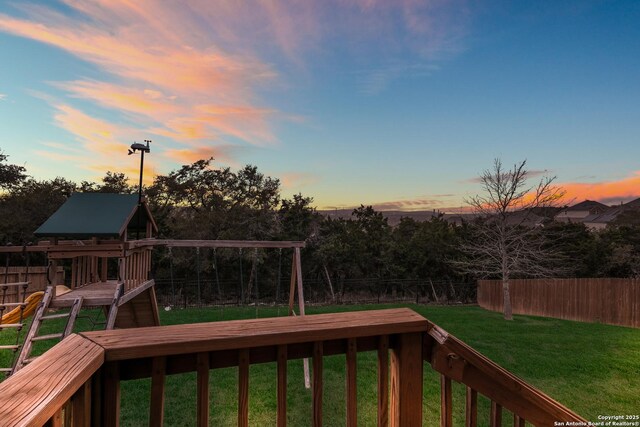 deck at dusk with a yard, a playground, and a fenced backyard