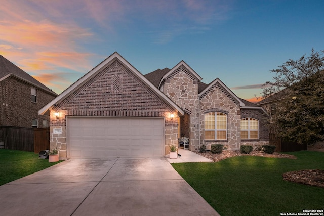 french country inspired facade featuring driveway, a garage, a lawn, stone siding, and brick siding