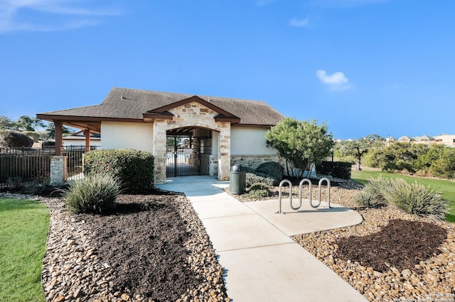 view of front of home with fence, stone siding, roof with shingles, a gate, and stucco siding