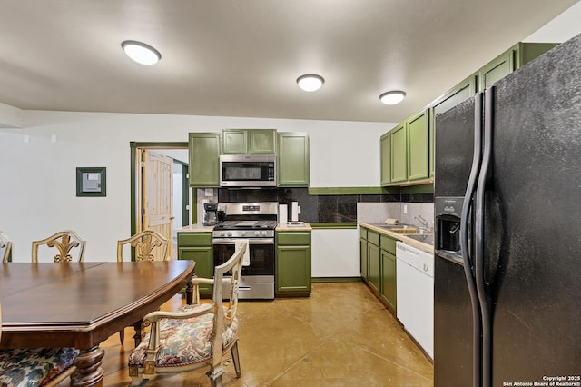 kitchen with green cabinetry, appliances with stainless steel finishes, backsplash, light countertops, and a sink