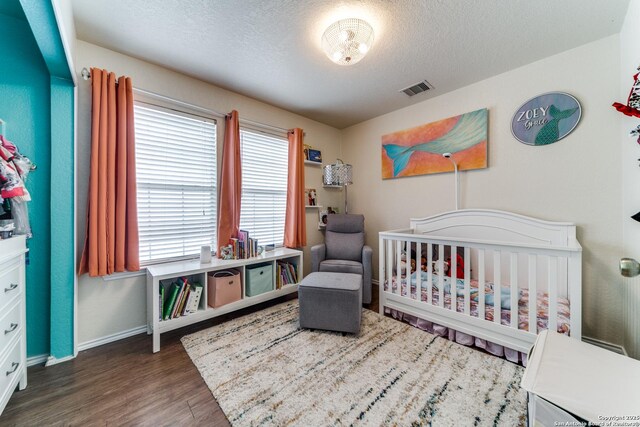 16110 Ambush Grv, San Antonio, TX 78247 - bedroom featuring wood finished floors, baseboards, visible vents, a crib, and a textured ceiling