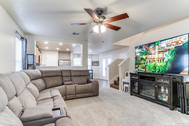 living area featuring visible vents, a ceiling fan, a glass covered fireplace, stairs, and carpet floors