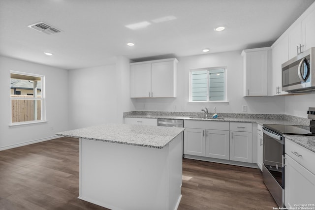 kitchen with visible vents, dark wood-type flooring, a center island, stainless steel appliances, and a sink