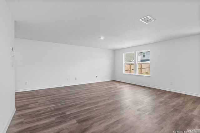empty room with baseboards, visible vents, and dark wood finished floors