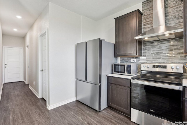 kitchen featuring dark wood-type flooring, stainless steel appliances, dark brown cabinets, wall chimney range hood, and backsplash