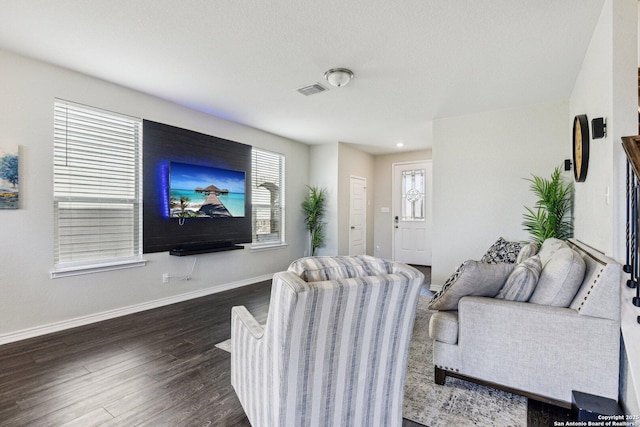 living room with dark wood-style flooring, visible vents, and baseboards