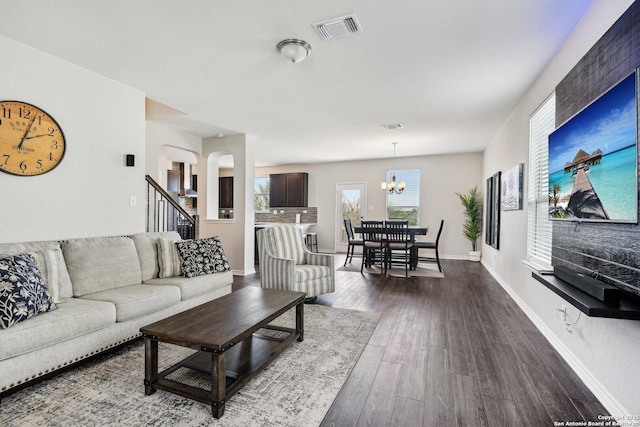 living area with a notable chandelier, dark wood-type flooring, visible vents, baseboards, and stairs