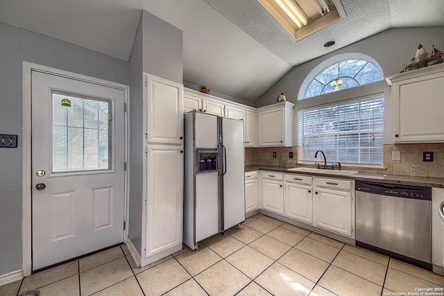 kitchen with light tile patterned floors, a sink, white fridge with ice dispenser, vaulted ceiling with skylight, and dishwasher