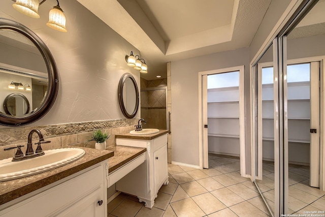 full bath featuring a raised ceiling, tile patterned floors, a sink, a spacious closet, and two vanities