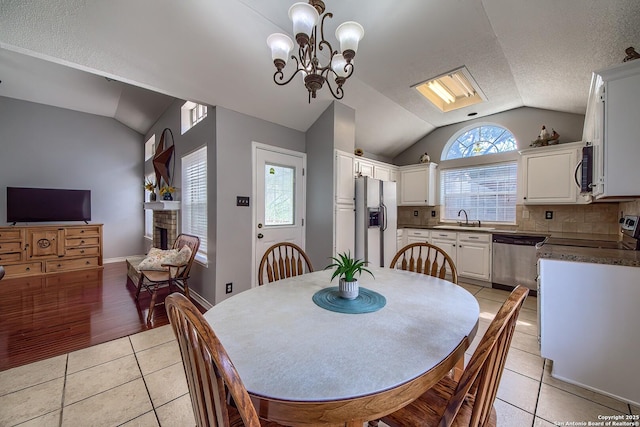 dining area featuring light tile patterned floors, a fireplace, a chandelier, and vaulted ceiling