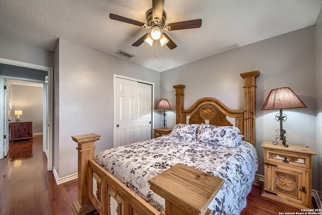 bedroom with a textured ceiling, dark wood-type flooring, visible vents, baseboards, and a closet