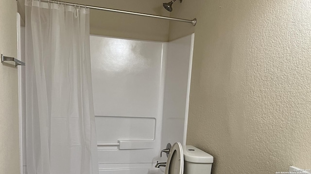 full bathroom with toilet, a shower with curtain, and a textured wall