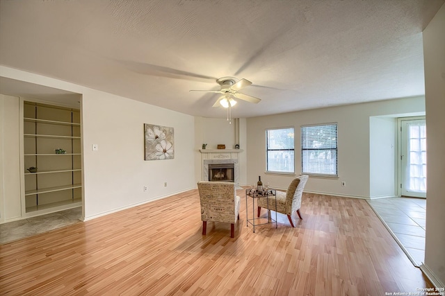 sitting room featuring ceiling fan, a textured ceiling, light wood-type flooring, and a tile fireplace