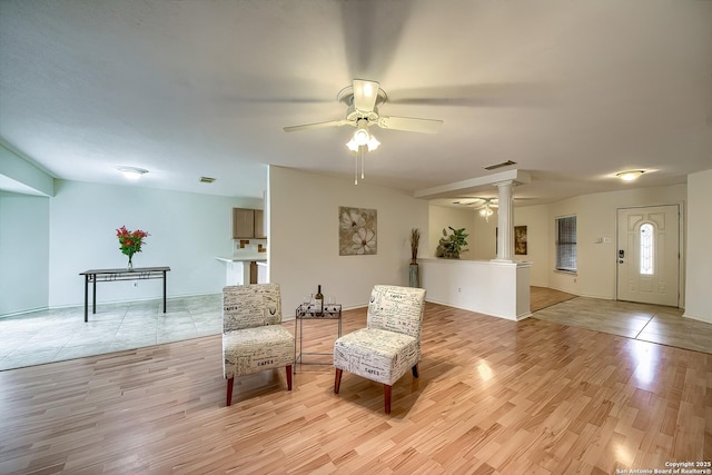 sitting room with ornate columns, visible vents, a ceiling fan, and light wood-style floors