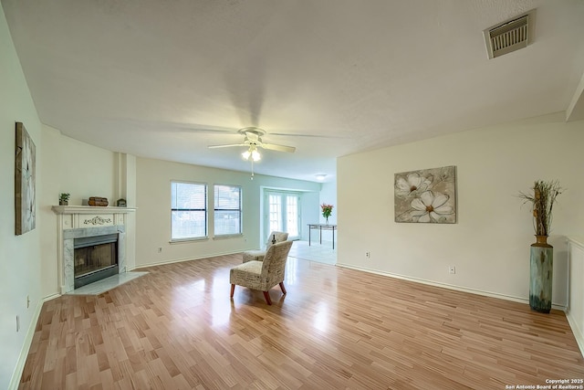 unfurnished room with light wood finished floors, ceiling fan, a fireplace, and visible vents