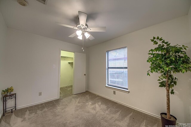 unfurnished bedroom featuring a ceiling fan, a walk in closet, and carpet flooring