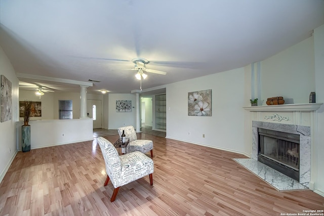 living area with decorative columns, a premium fireplace, a ceiling fan, and wood finished floors