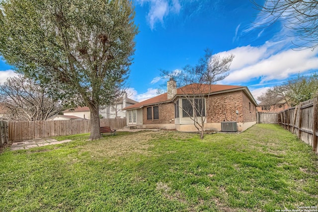 back of house with a lawn, a fenced backyard, a chimney, central AC, and brick siding