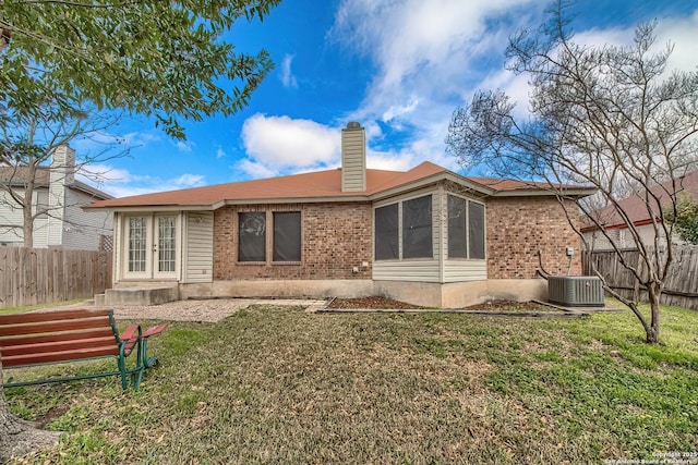 rear view of house with brick siding, a chimney, a lawn, central AC unit, and fence