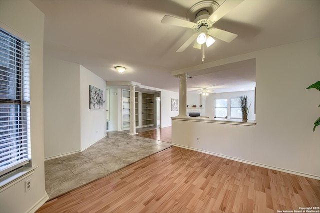 unfurnished room featuring baseboards, ceiling fan, light wood finished floors, and ornate columns