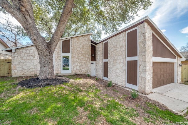 view of front of house with driveway, stone siding, an attached garage, and fence